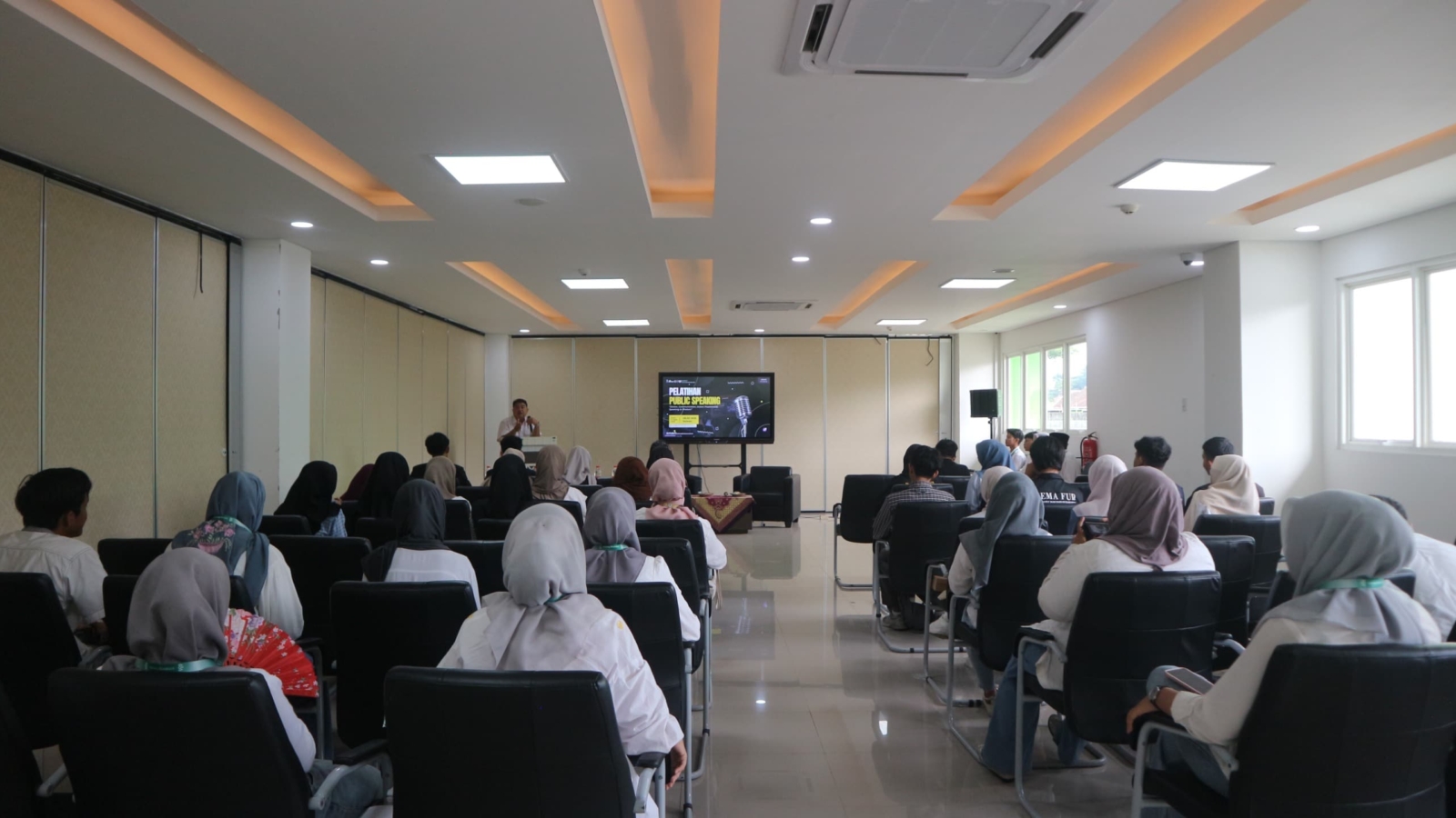 Suasana pelatihan public speaking di Aula FEBI UIN Raden Mas Said Surakarta, menampilkan narasumber Ayuniendra Fourtina Annisa sedang menyampaikan materi dengan peserta antusias mendengarkan dan mencatat, serta backdrop bertuliskan tema kegiatan.