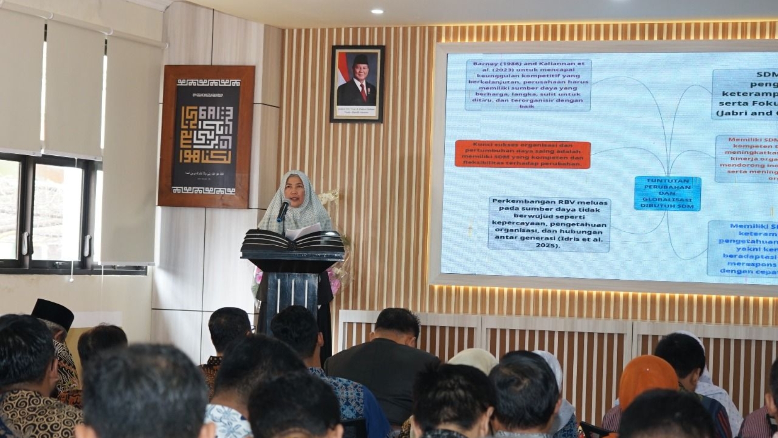 Prof. Dr. Fitri Wulandari tengah memaparkan materi orasi ilmiah di Aula FEBI UIN Raden Mas Said Surakarta, dengan latar slide presentasi bertema Manajemen Sumber Daya Manusia dan nuansa akademik yang khidmat.